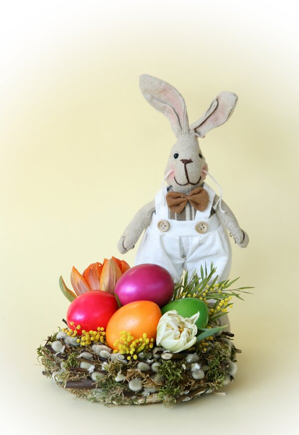 Bild vergr&ouml;&szlig;ern: Das Bild zeigt eine Osterdekoration, die einen Stoffhasen und mehrere bunter Eier in einem Nest.